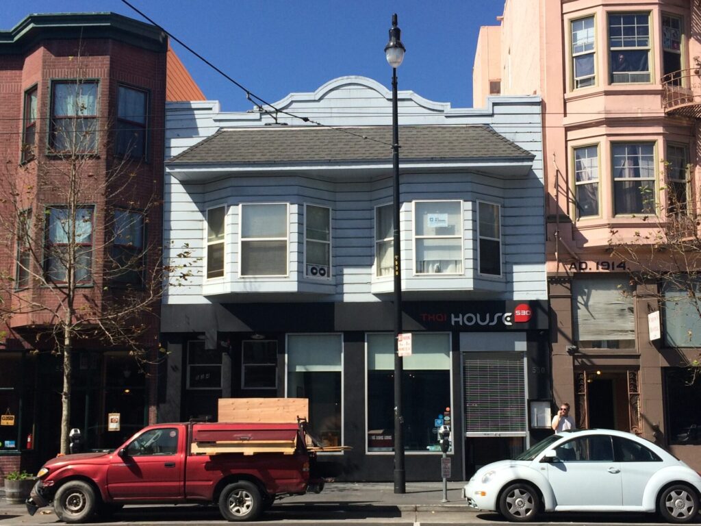A modern daytime photo of a two-story building with bay windows and a gray facade, with a business called “HOUSE” on the ground floor.